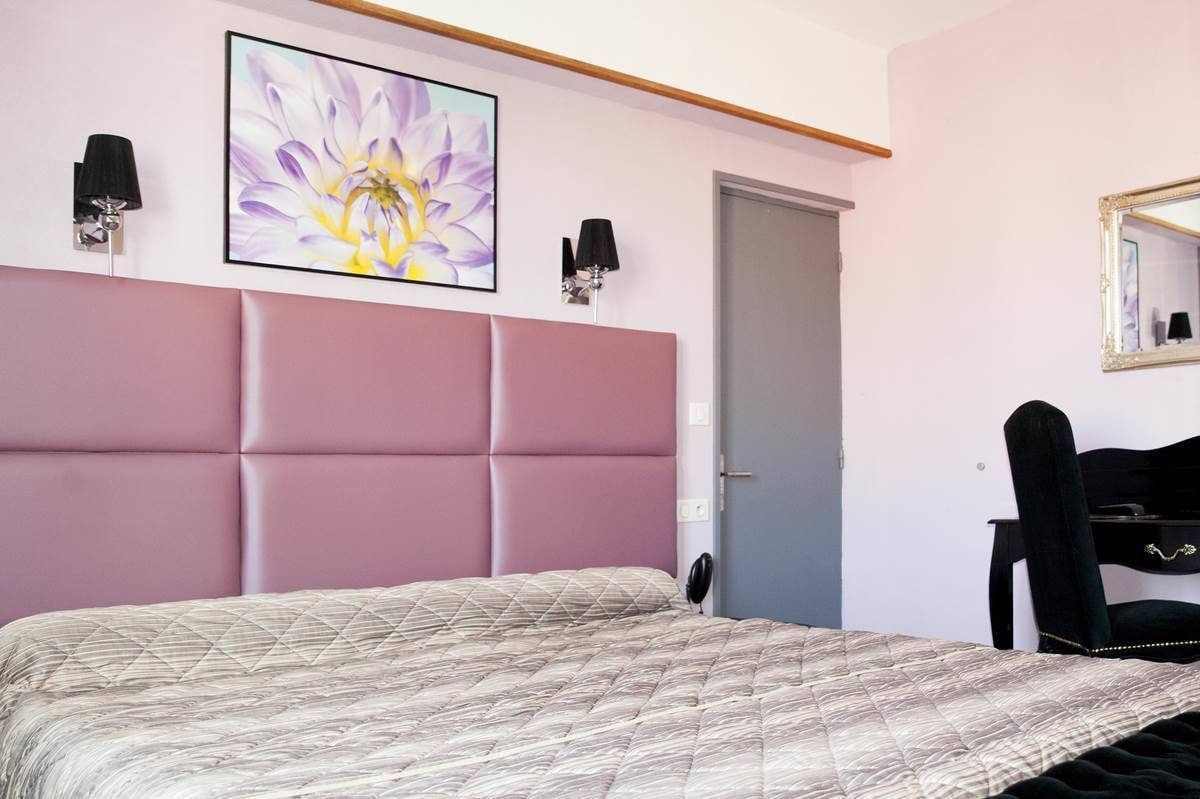 Un dormitorio con una cama grande, cabecera, dos lámparas de pared, una puerta, un espejo y una silla.