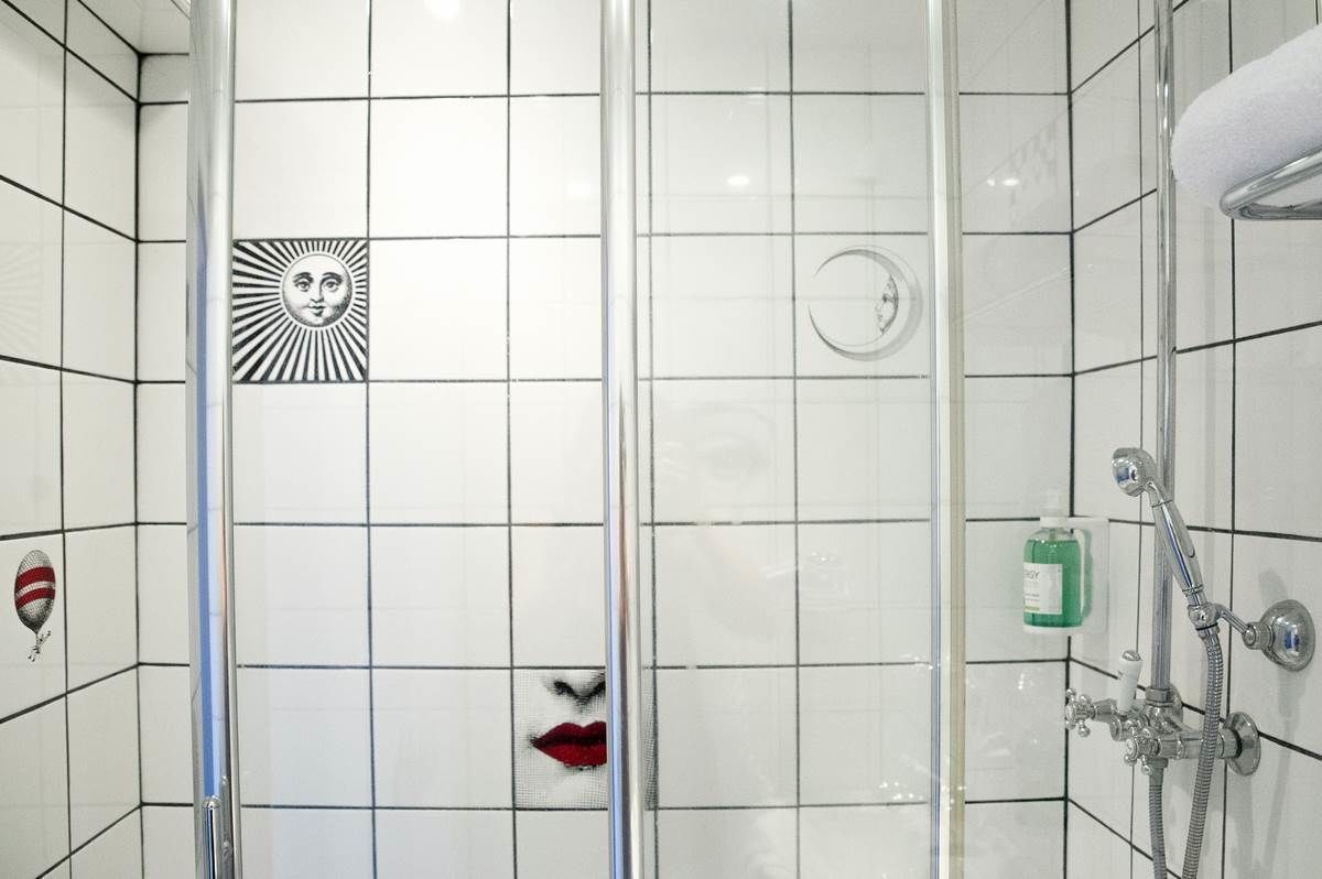 A tiled shower area with a glass partition, a hand dryer, and a soap dispenser.
