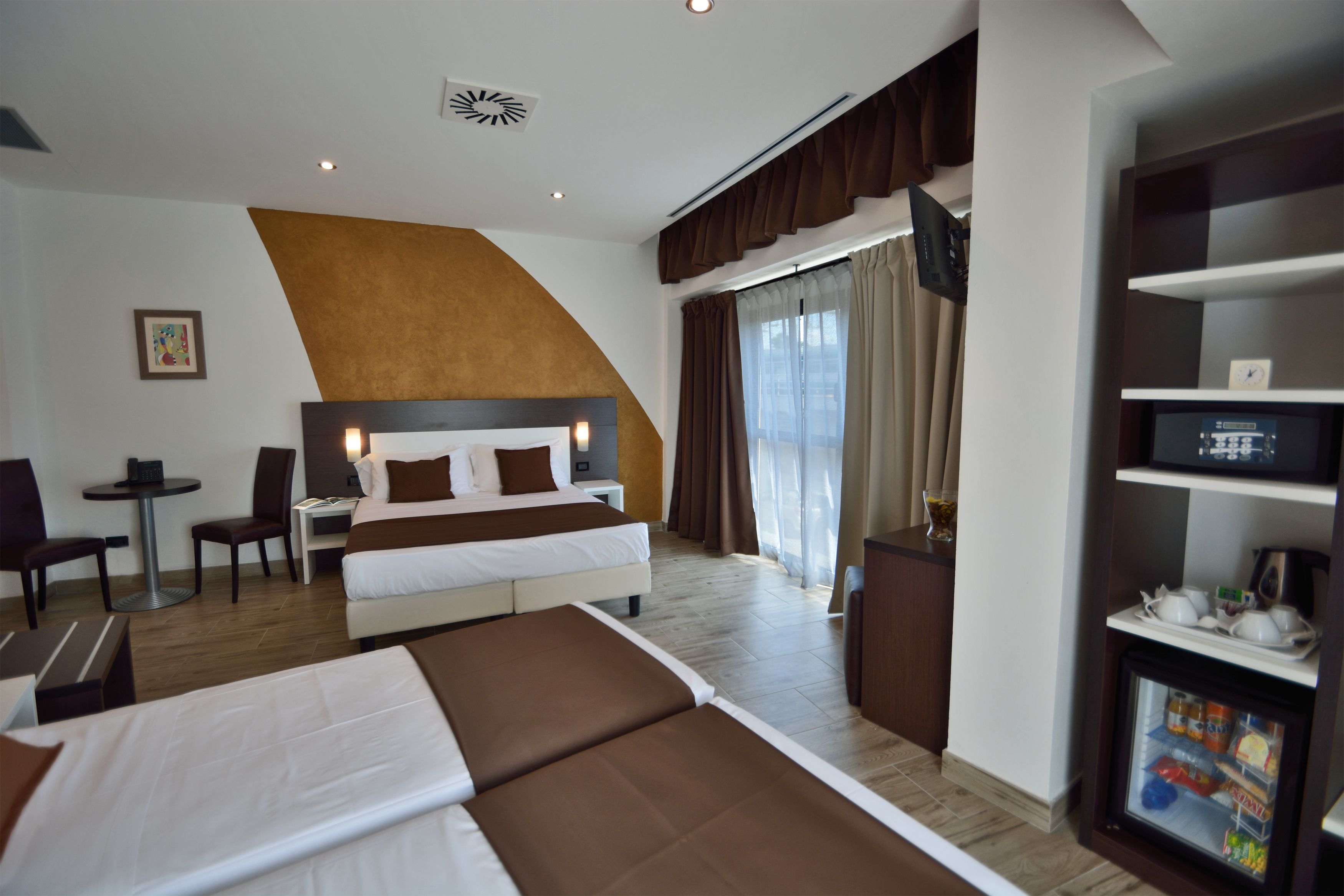 A hotel room with a large bed, a desk, a chair, a TV, and a minibar.