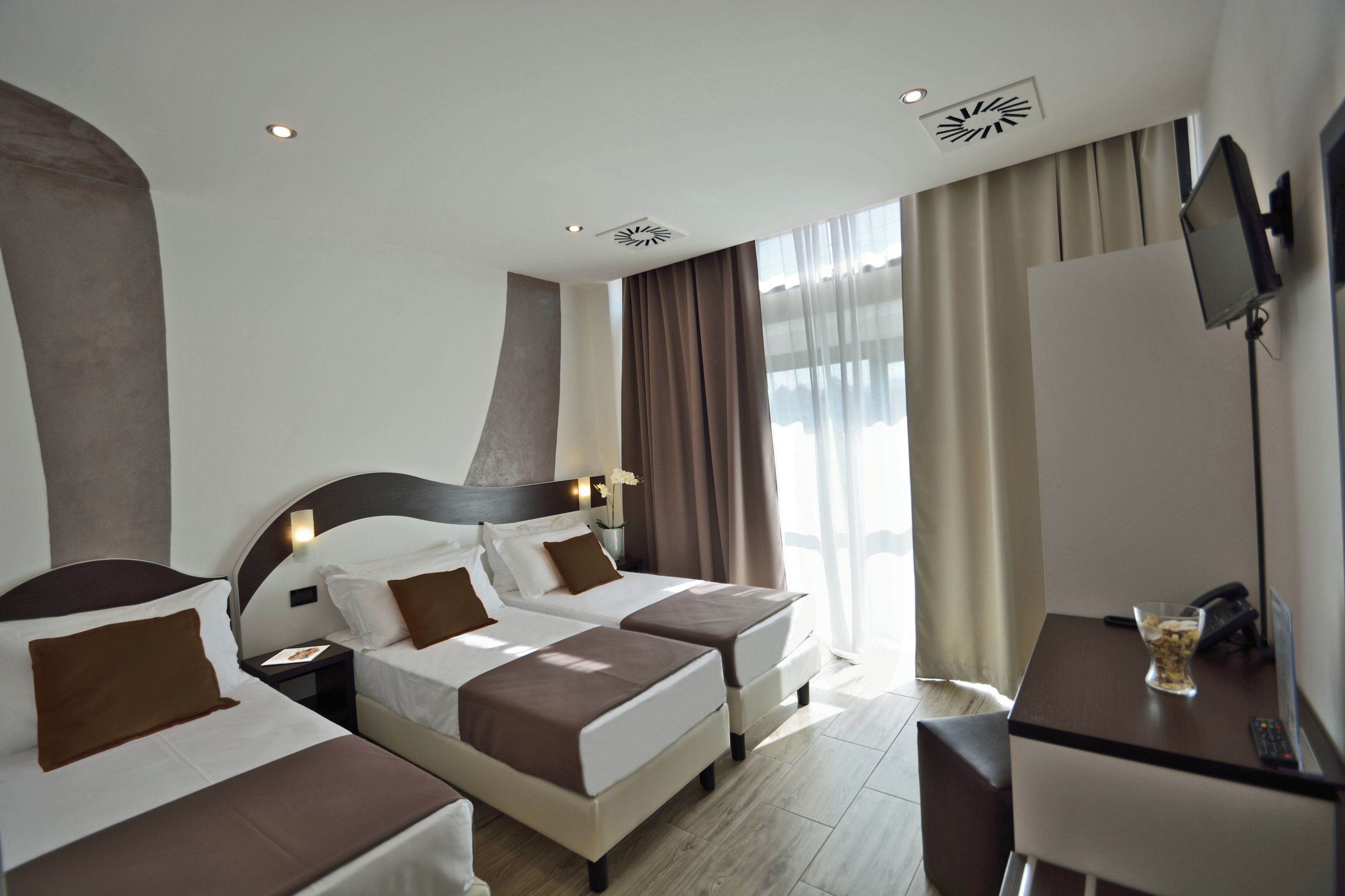 A hotel room with two beds, a desk, a TV, and a window with curtains.