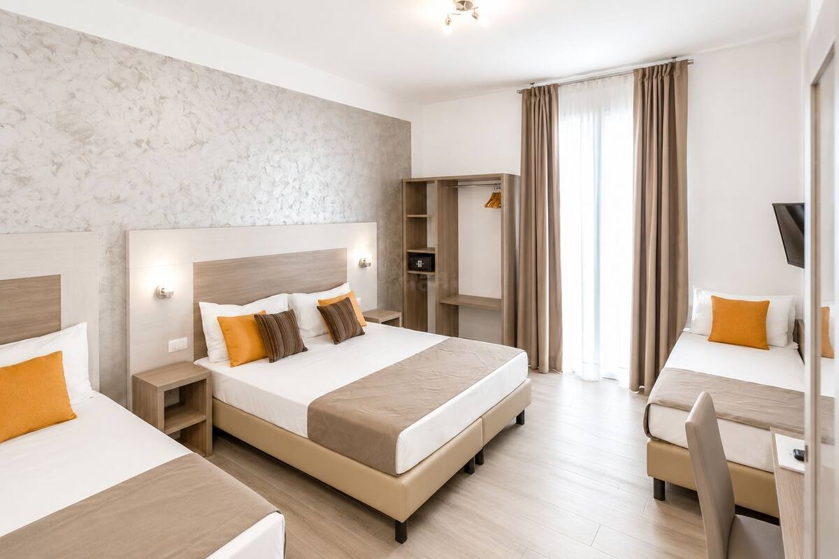 Een hotelkamer met een groot bed, een kleiner bed, een bureau met stoel, een kledingkast en een televisie.