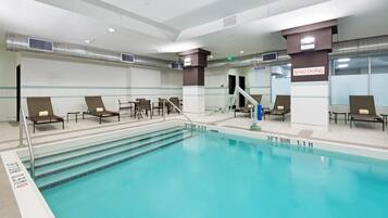 Una piscina interior con marcas de carriles claras, sillas de descanso y un cartel de prohibido bucear.