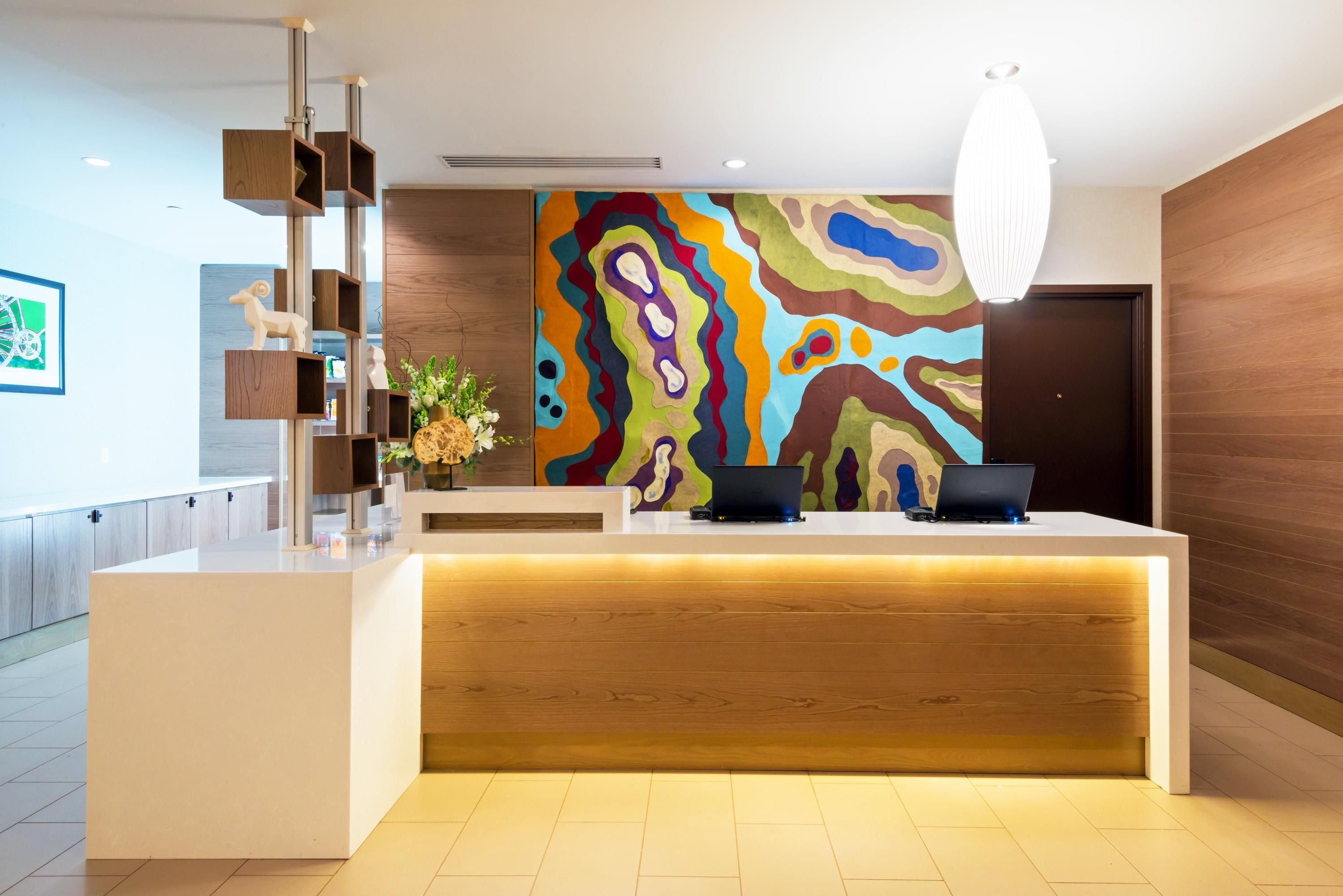 A modern reception desk with a colorful abstract painting, wooden accents, and a laptop on the counter.