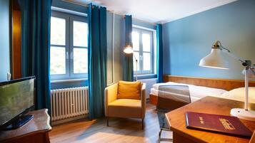 A hotel room with a bed, a chair, a desk with a lamp, a TV, and a window with curtains.
