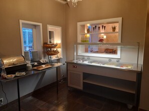 A breakfast bar with a coffee machine, a bread basket, and a display case with food items.