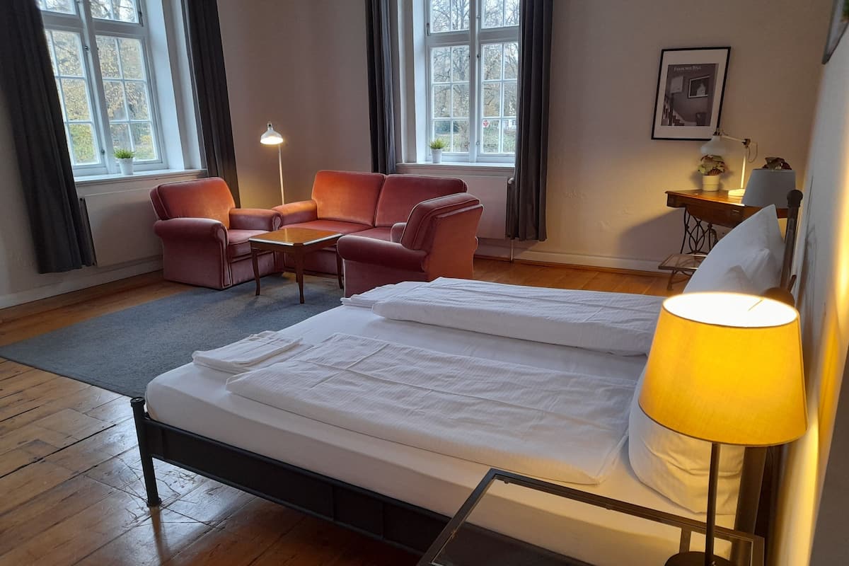 A hotel room with a bed, a desk, a chair, and two windows.