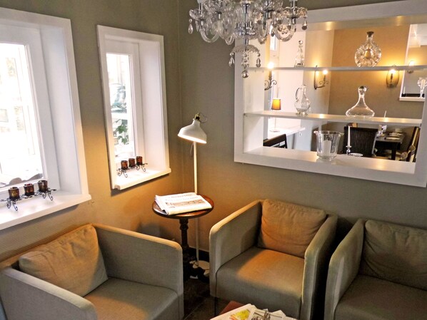 A cozy living room with two armchairs, a small table with a lamp, a window with a shelf of candles, and a mirror reflecting a dining area. - Hotel Pelli Hof Rendsburg by Tulip Inn (Rendsburg)