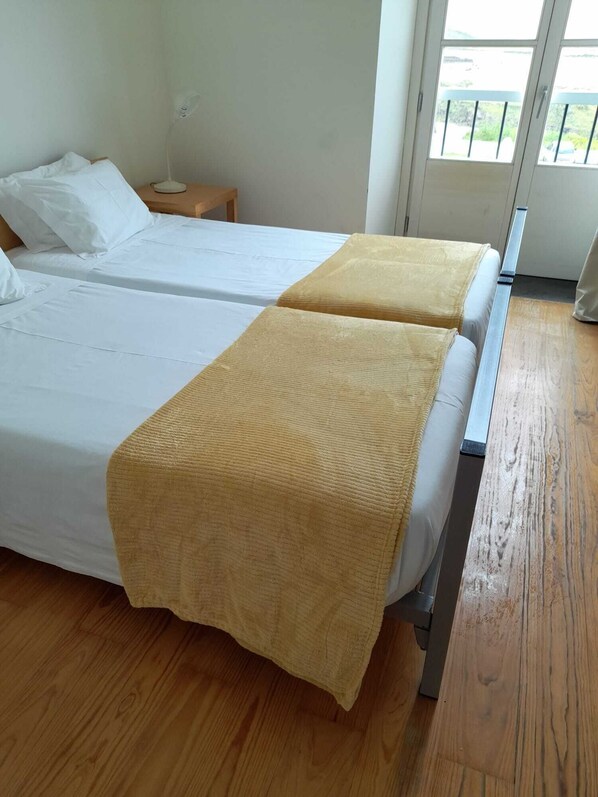 Une chambre avec deux lits, un plancher en bois, une table de chevet et une fenêtre donnant sur un beau paysage.