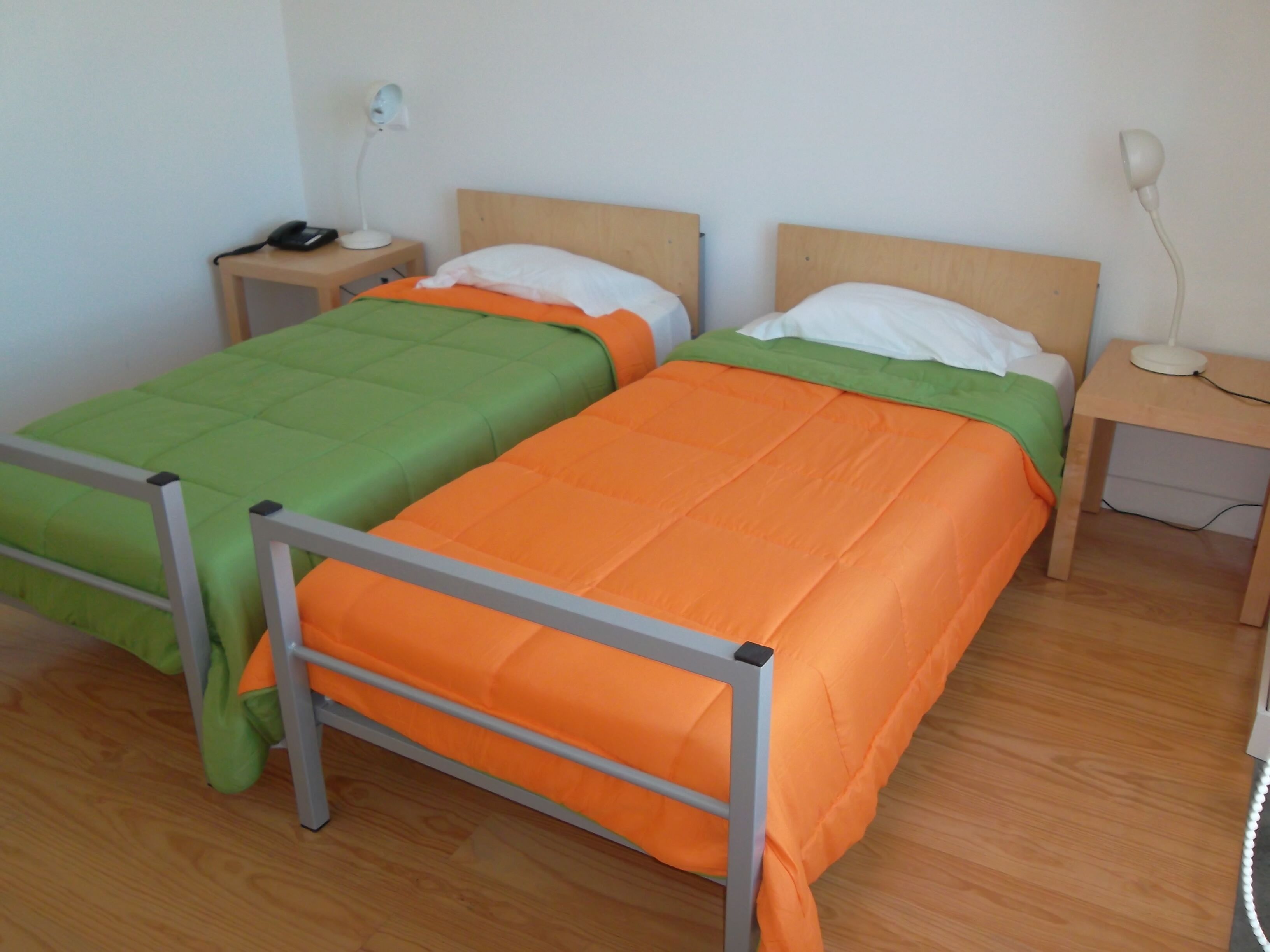Two single beds with metal frames, wooden headboards, and bedside tables with lamps.
