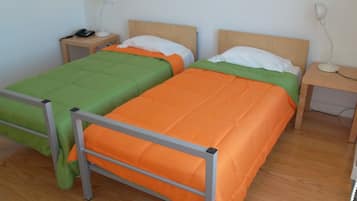 Two single beds with metal frames, wooden headboards, and bedside tables with lamps.