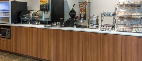 A breakfast bar with a coffee machine, waffle maker, and refrigerated display.