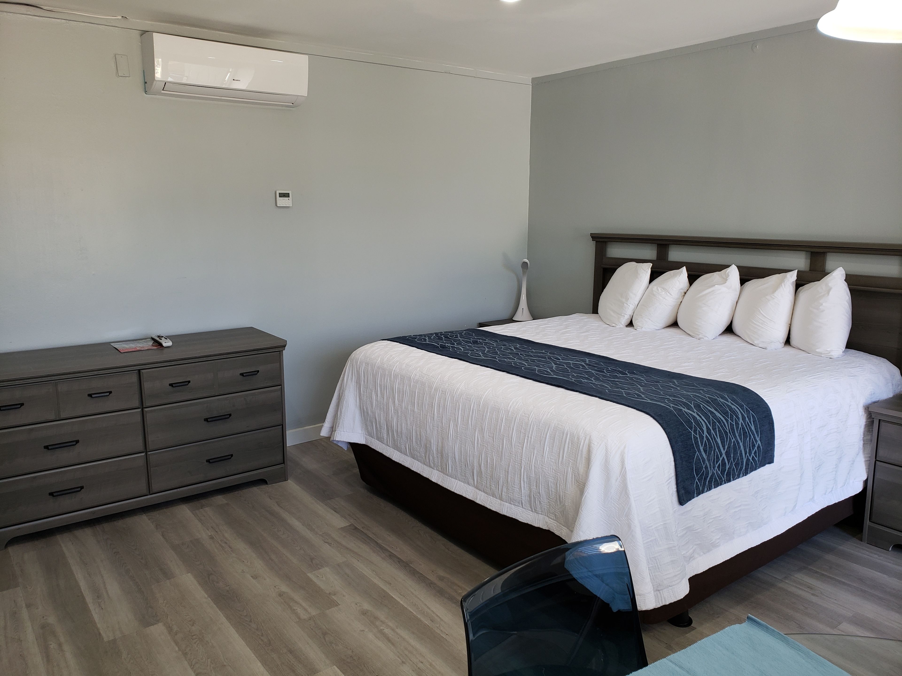 Un dormitorio con cama, cómoda, mesita de noche y un equipo de aire acondicionado.