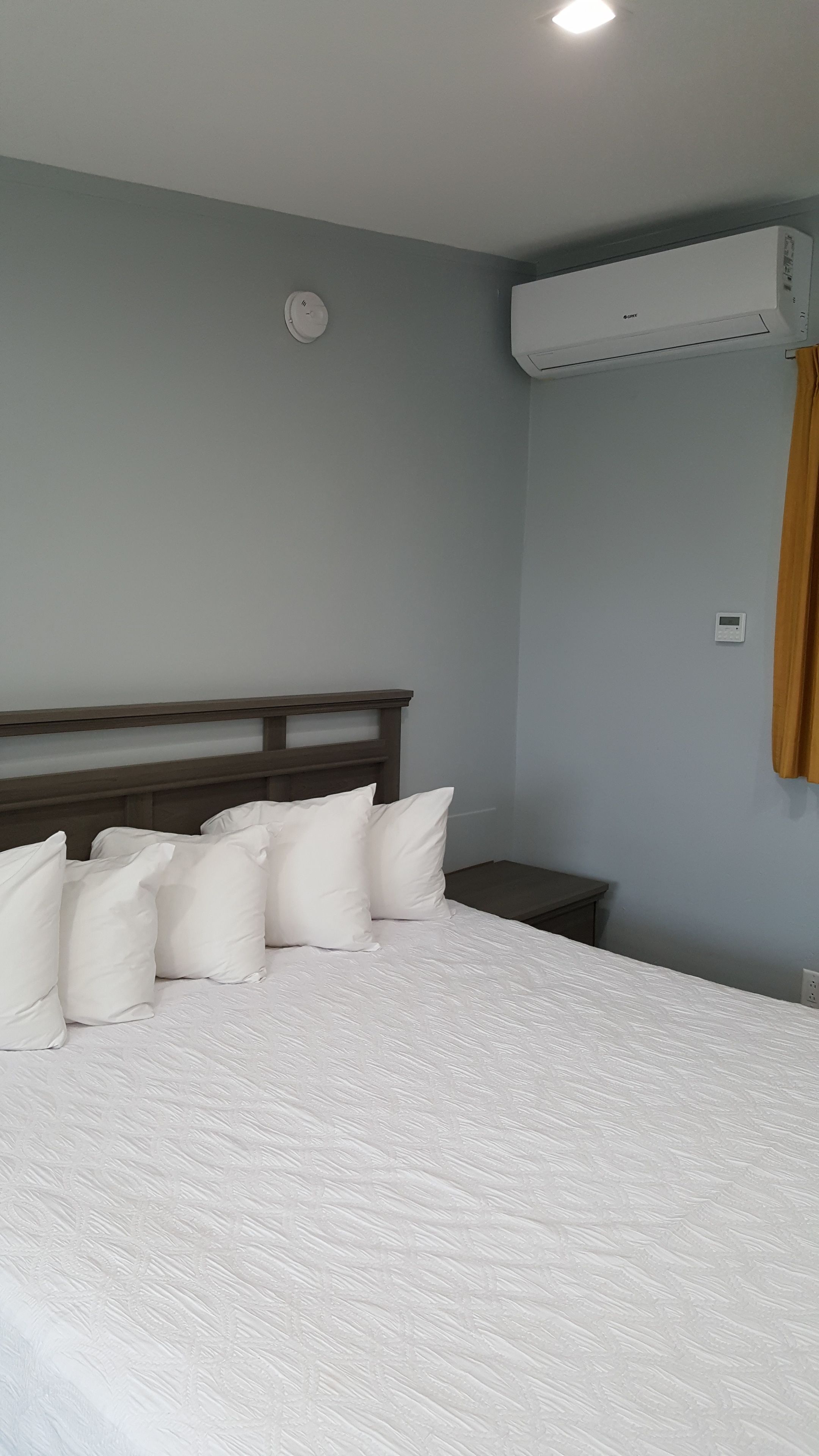 Ein Schlafzimmer mit einem Bett, einem Nachttisch, einer Wand-Klimaanlage und einem Rauchmelder.