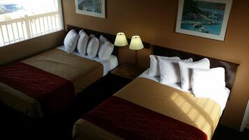Habitación de hotel con dos camas, cada una con ropa blanca de cama y almohadas, una colcha rojo y beige, y una mesita de noche con dos lámparas.