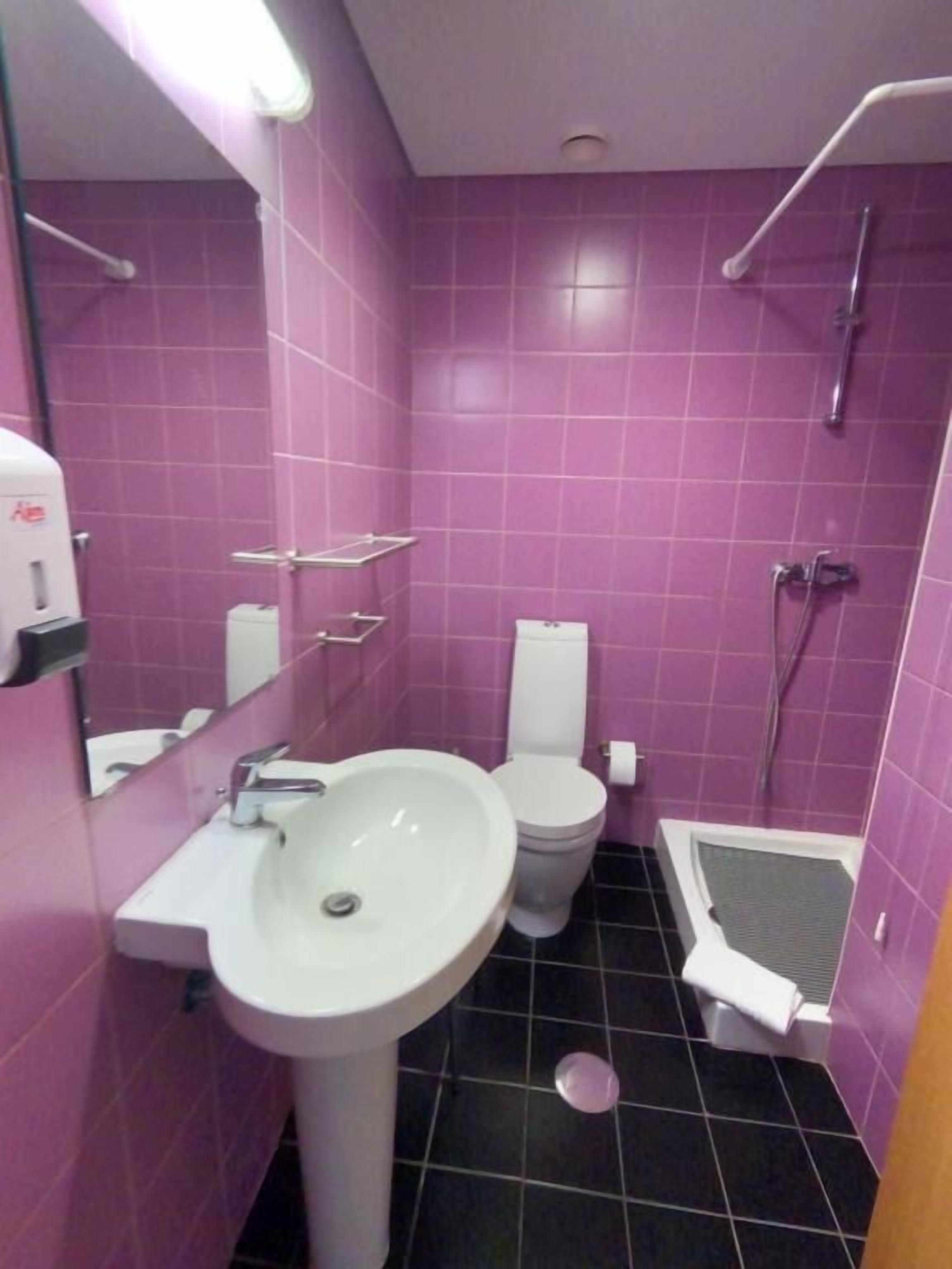 A bathroom with purple tiles, a white sink, a toilet, and a shower area.