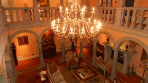 Un interior imponente con una gran araña, muebles ornamentados y un balcón con barandilla.