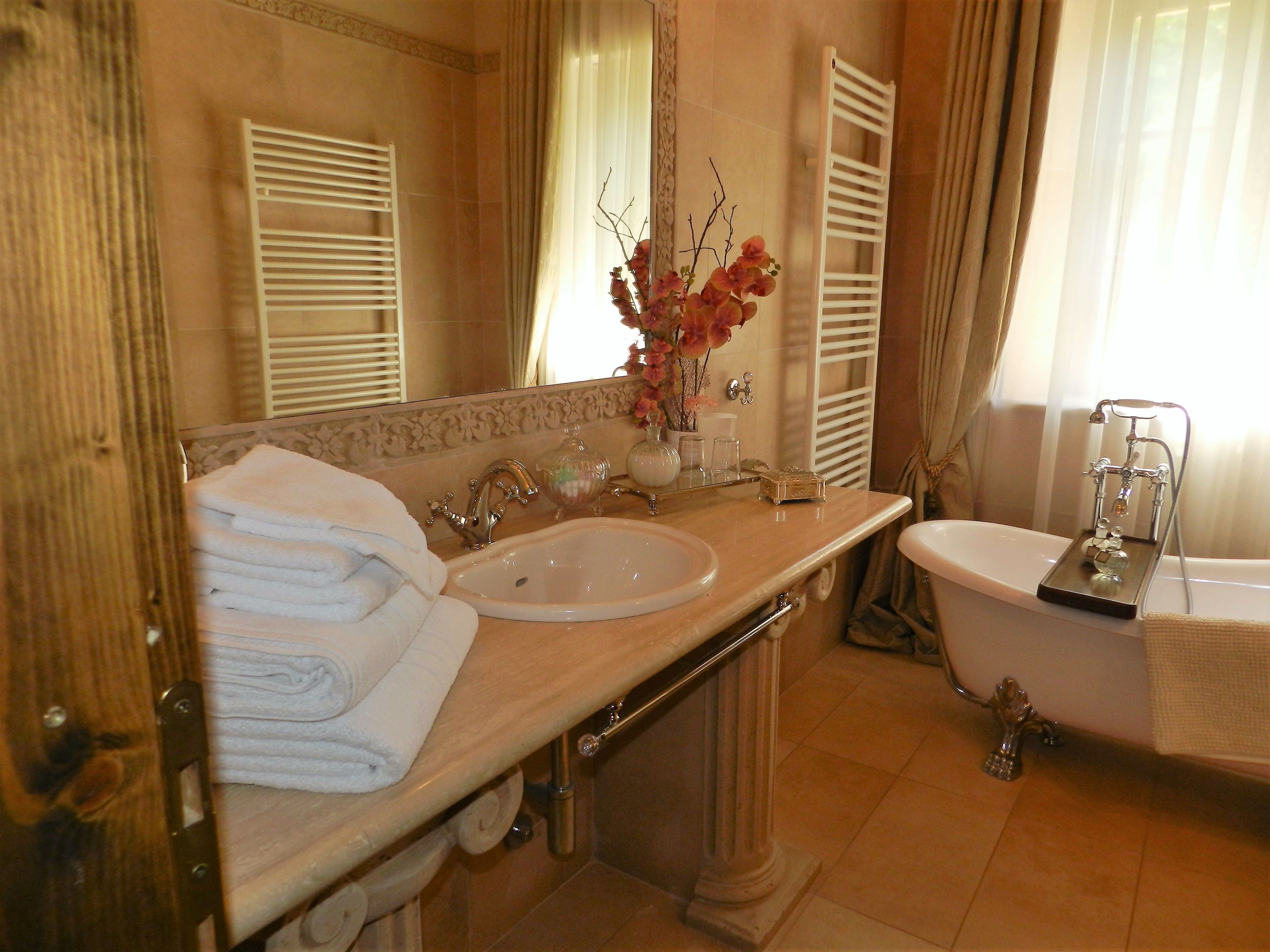 A bathroom with a sink, mirror, and bathtub. There are towels stacked on the left side and a vase with flowers on the sink.