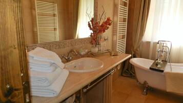 A bathroom with a sink, mirror, and bathtub. There are towels stacked on the left side and a vase with flowers on the sink.