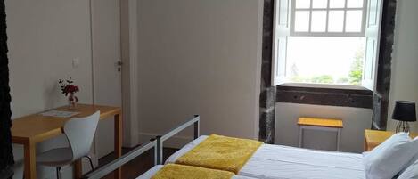 Ein Hotelzimmer mit Bett, Schreibtisch, Stuhl, Fernseher und einem Fenster mit Blick auf Grünflächen.