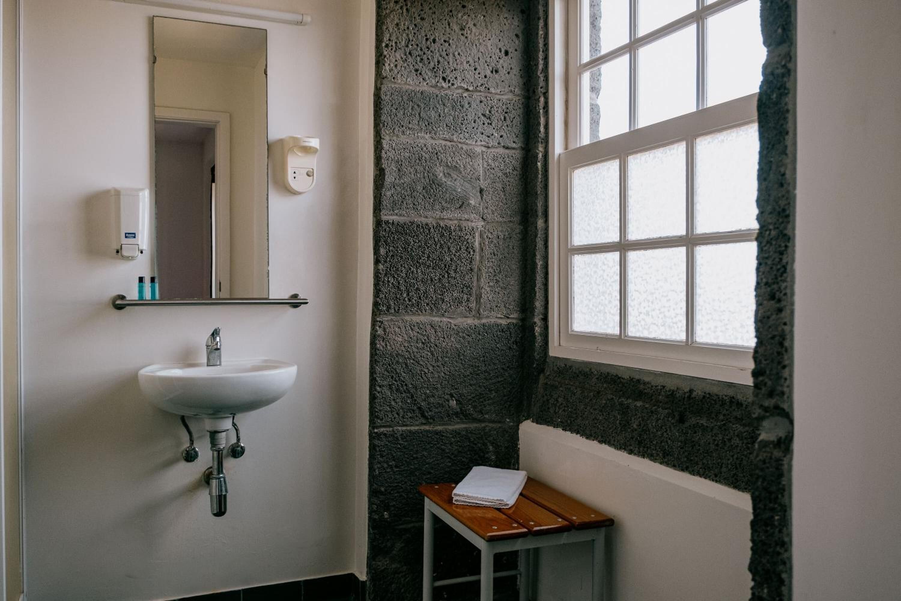 A bathroom with a white sink, a mirror, a soap dispenser, and a window with frosted glass.