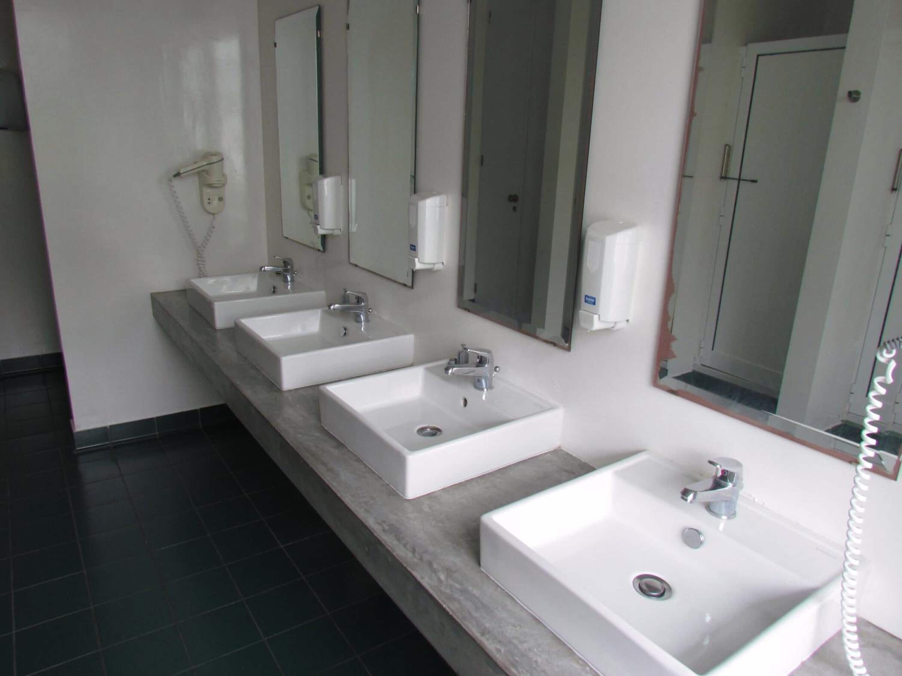 Un baño moderno con tres lavamanos, un secador de pelo y un teléfono.