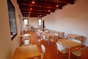 Enjoy meals in this dining area with high ceilings and wooden beams, featuring multiple tables and chairs for groups.