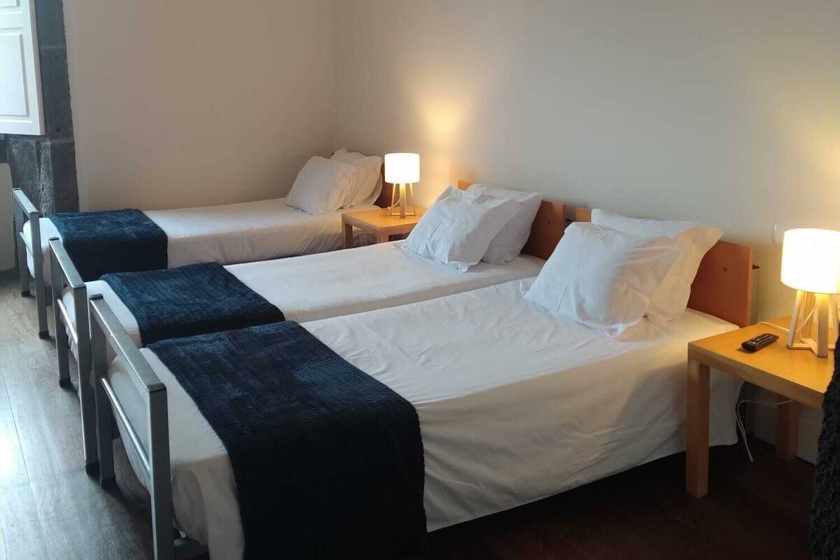 Een hotelkamer met twee eenpersoonsbedden, een houten vloer, een nachtkastje met een lamp en een raam met gordijnen.