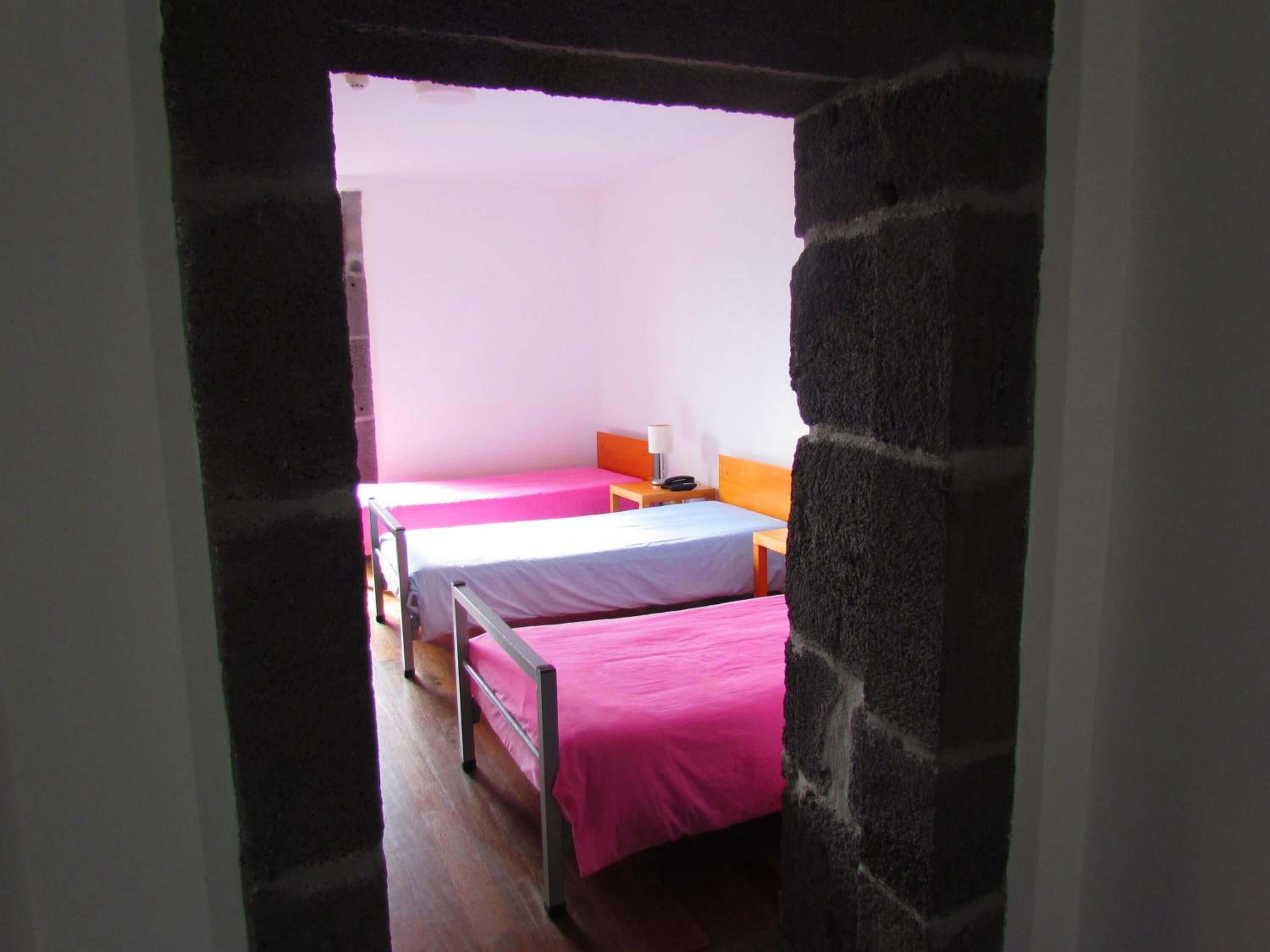 Una camera del dormitorio con due letti, ciascuno con copriletto rosa, un comodino in legno e una lampada. La stanza ha pareti bianche e pavimento in legno.