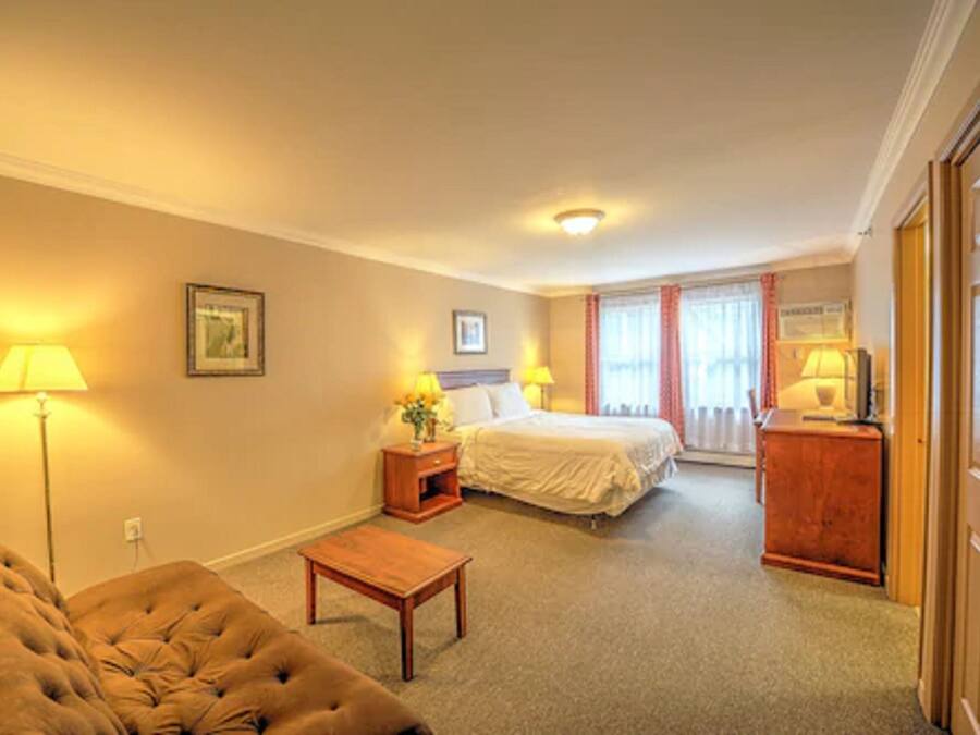 A hotel room with a bed, a bedside table with a lamp, a small table, and a chair.
