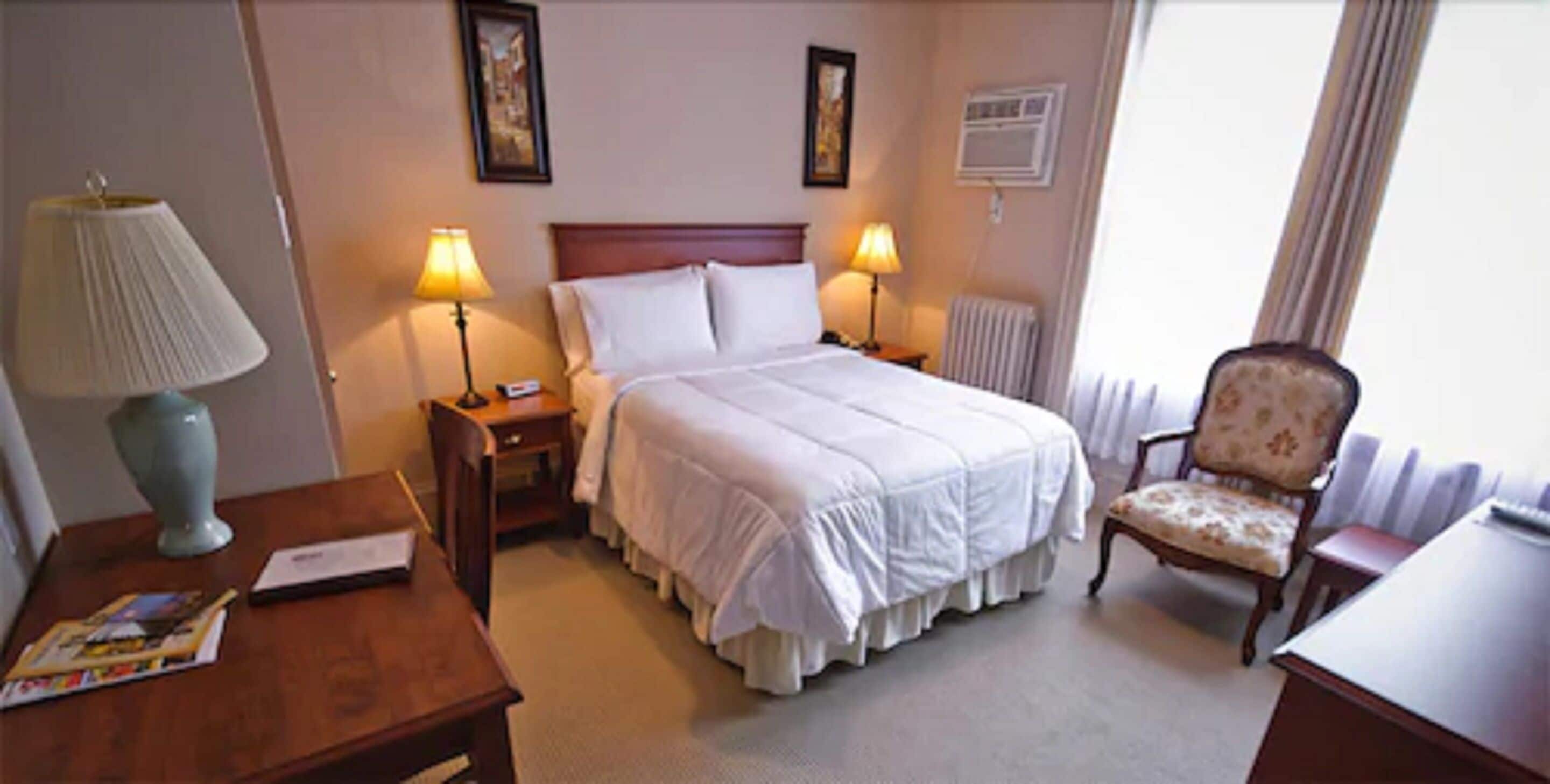 Una habitación de hotel con una cama, dos mesitas de noche con lámparas, una silla y un escritorio.