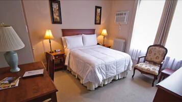 Una habitación de hotel con una cama, dos mesitas de noche con lámparas, una silla y un escritorio.
