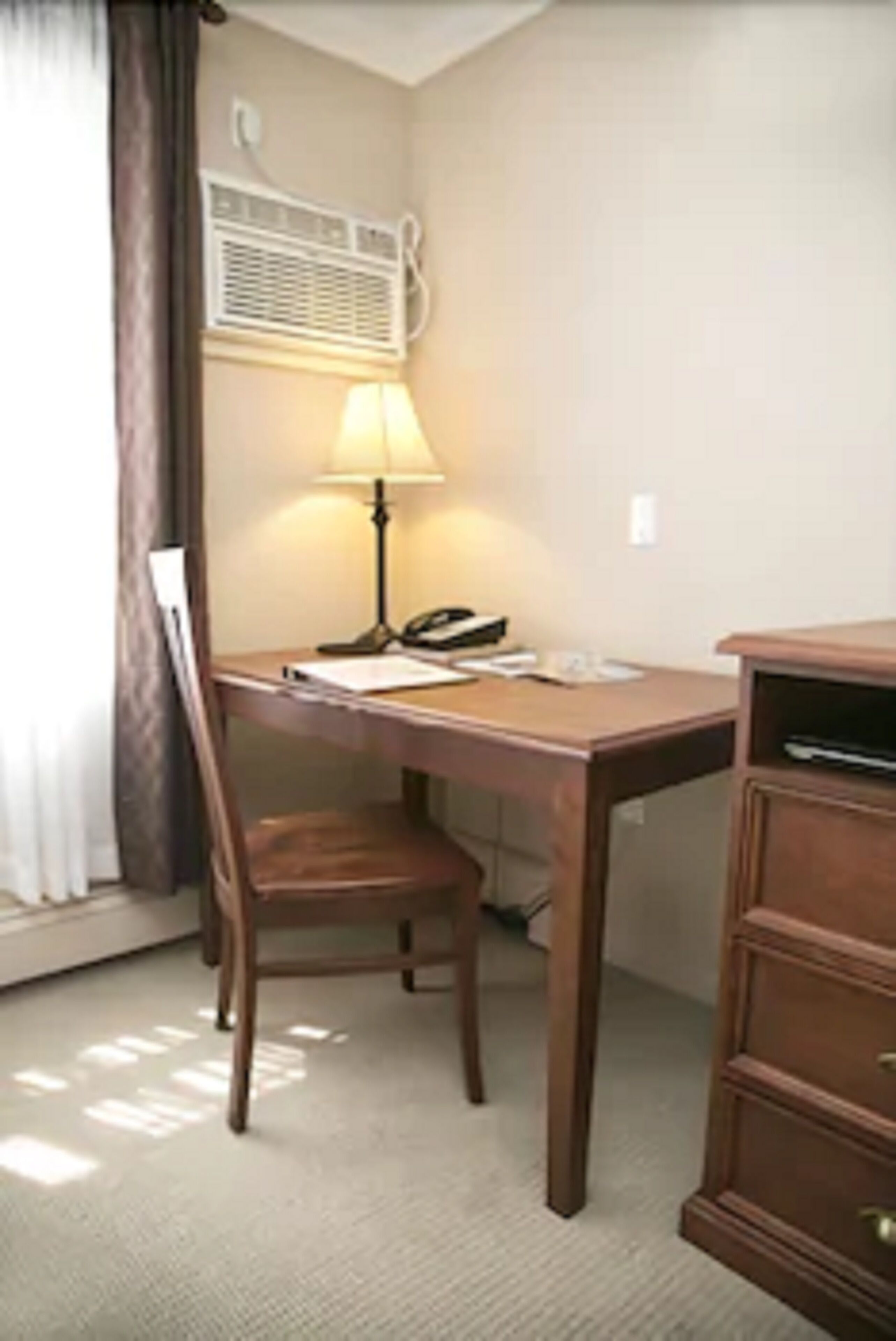 Een hotelkamer met een houten bureau, een lamp, een telefoon en een archiefkast.