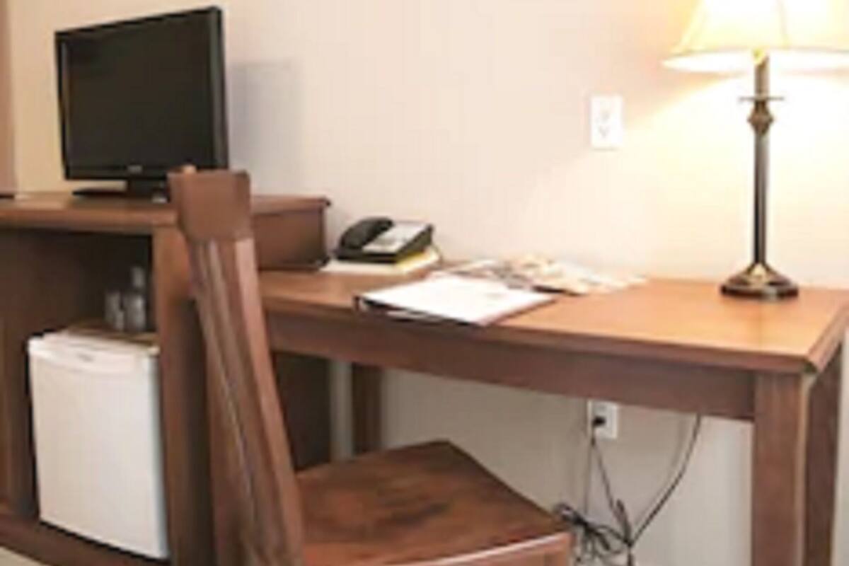 A small, neatly arranged office space with a wooden desk, a chair, a lamp, a computer monitor, and a small refrigerator.