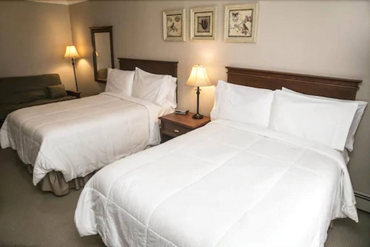 A hotel room with two beds, a nightstand, a lamp, and a wall-mounted mirror.