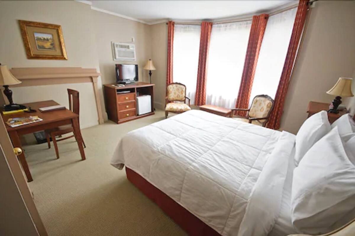 A hotel room with a bed, desk, chair, television, and curtains.