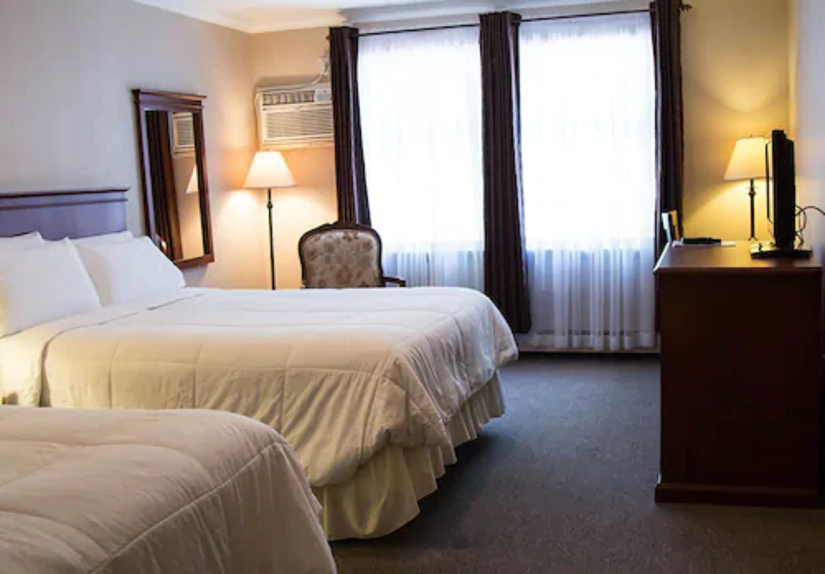 Een hotelkamer met twee bedden, een bureau, een stoel en een groot raam met gordijnen.