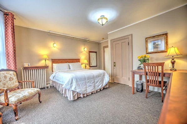 Une chambre d’hôtel avec un lit, une chaise, un bureau et un radiateur.