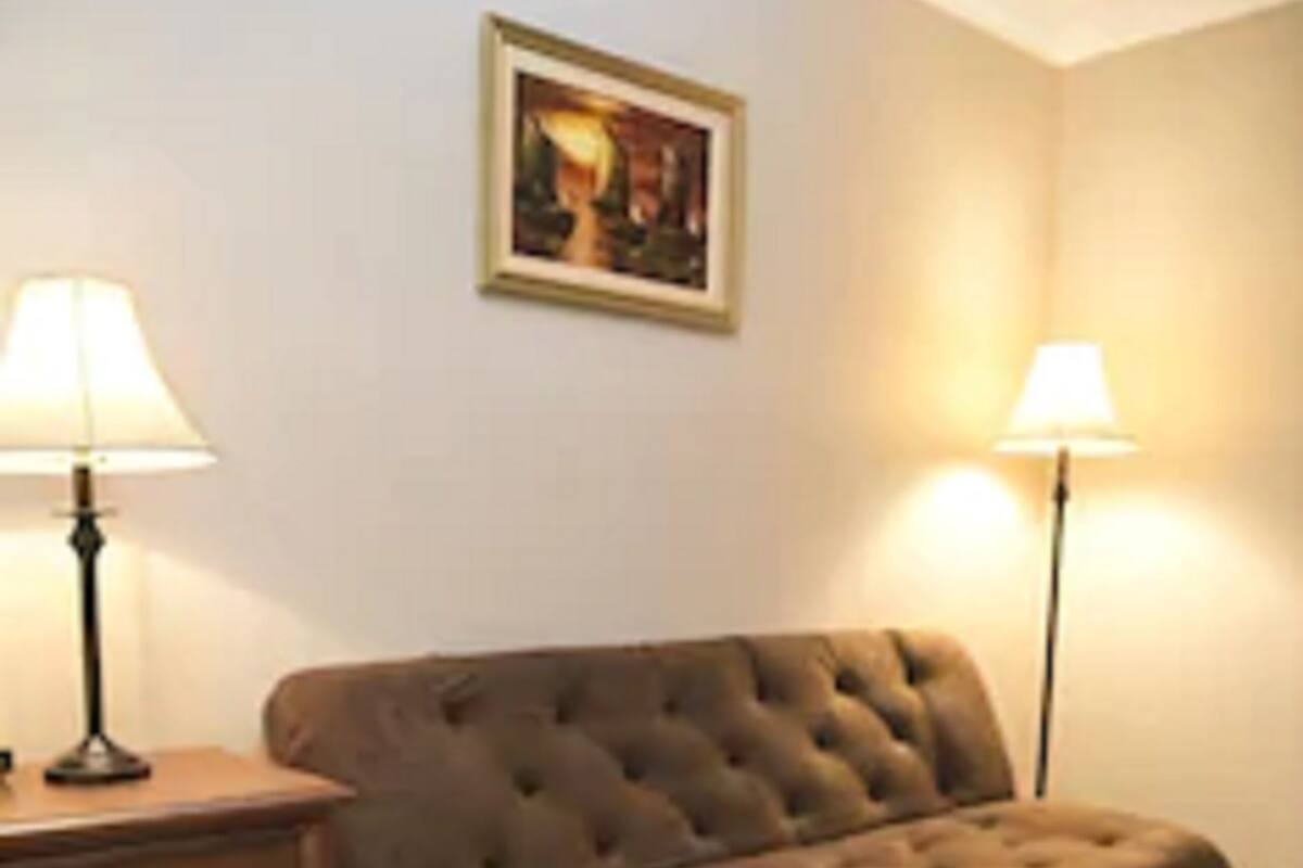 A living room with a brown sofa, two lamps, a small table, and a framed picture on the wall.