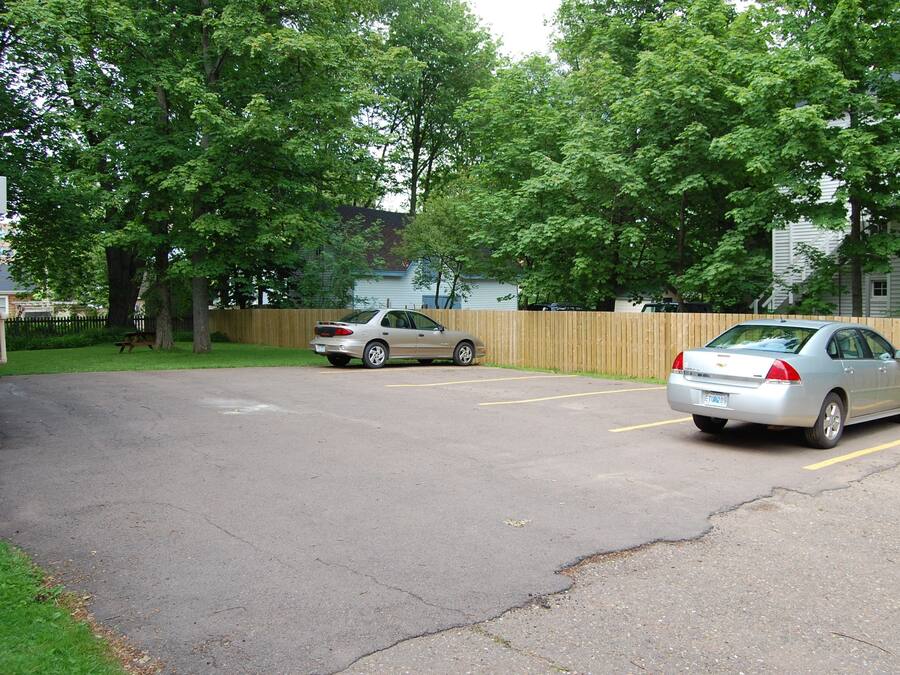 A parking lot with two cars and a wooden fence.