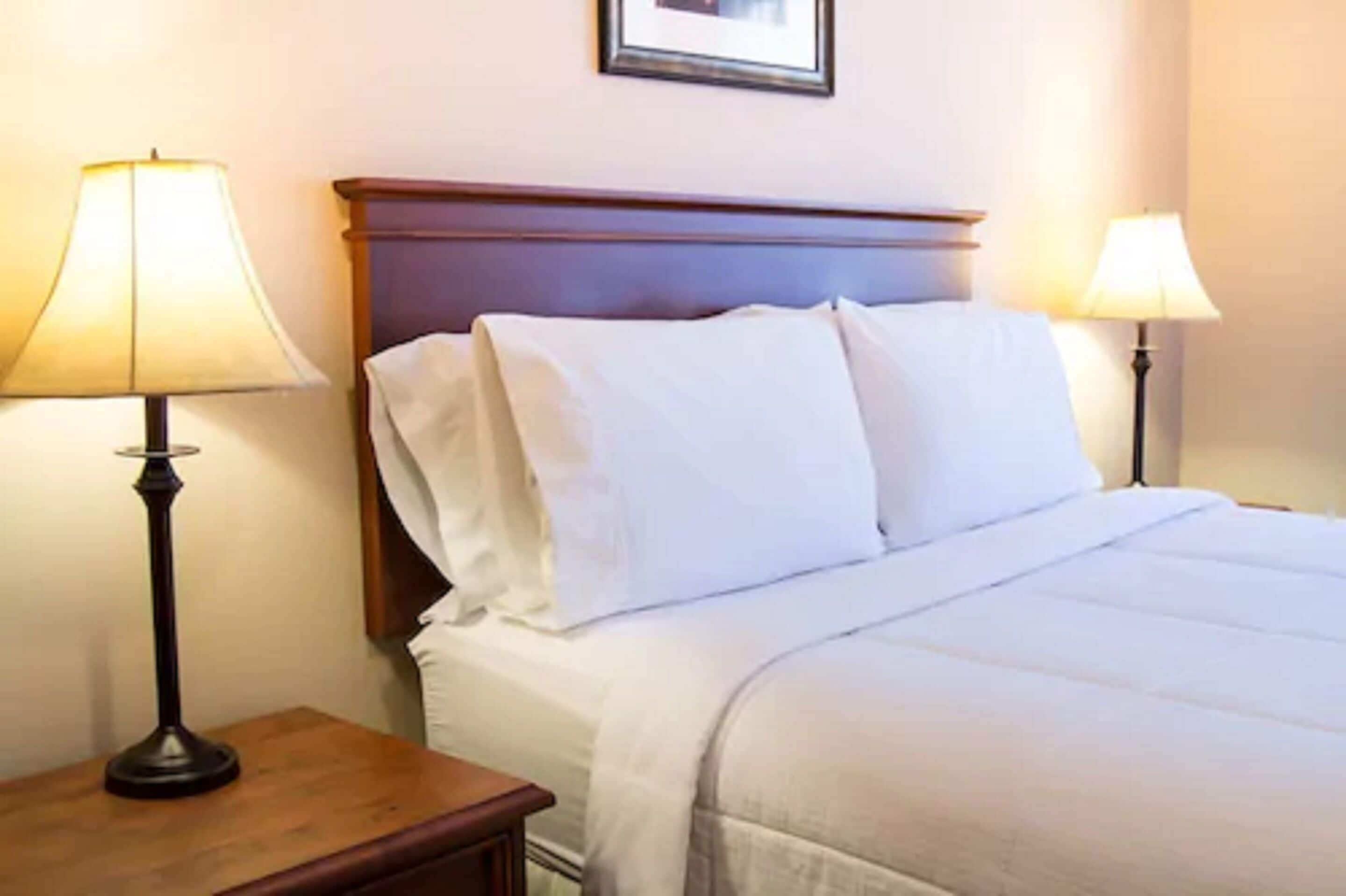 A neatly made bed with white linens, a wooden headboard, and two bedside lamps on wooden nightstands.