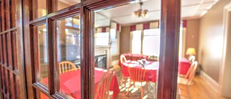 A dining area with a red table and chairs, a chandelier, and a carpeted floor.