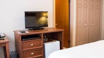 A hotel room with a bed, a wooden desk with a television, a mini-fridge, and a wardrobe.