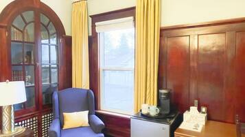 A room with a blue armchair, a wooden cabinet, a coffee machine, and a window with curtains.