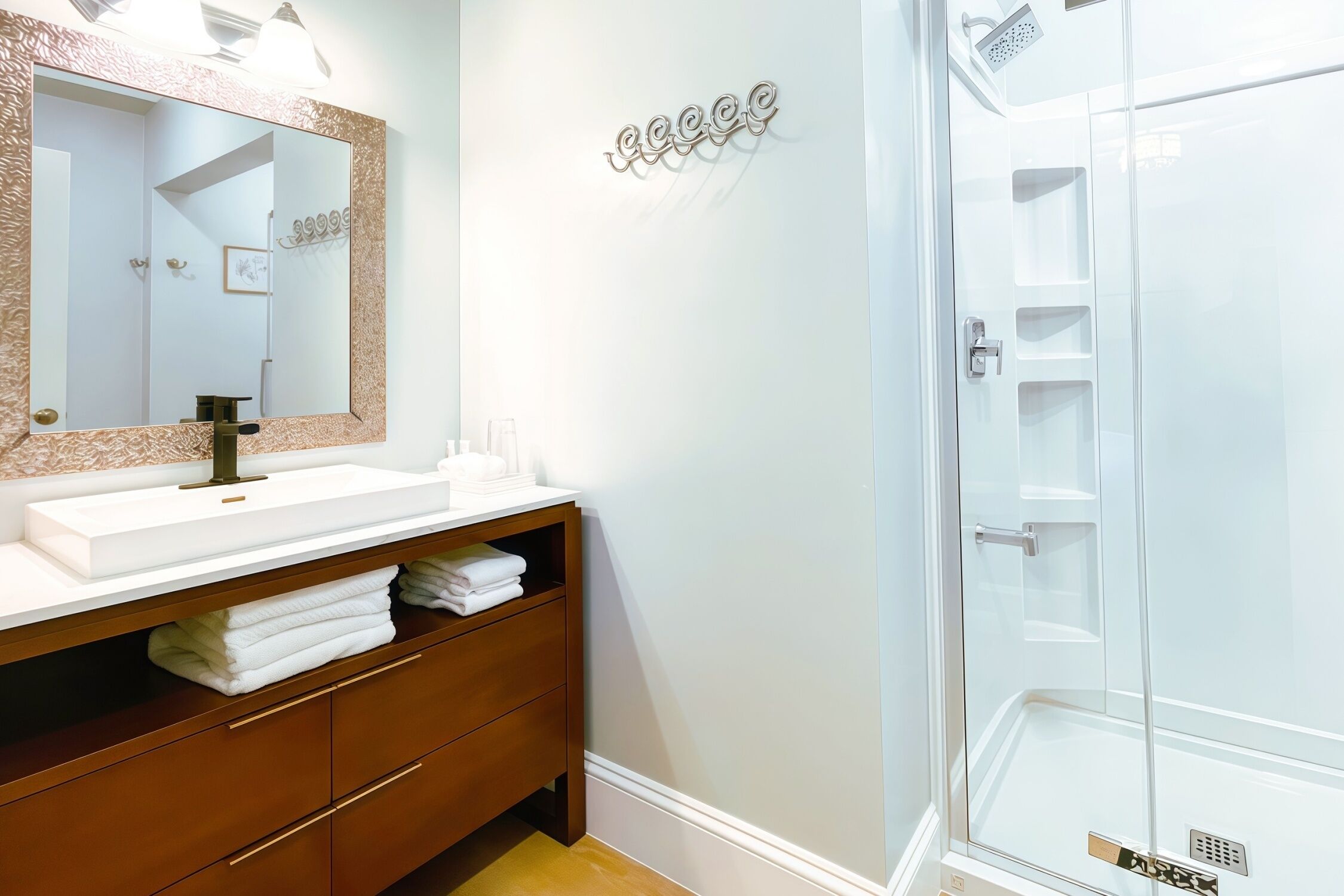Une salle de bain avec un lavabo blanc, un miroir doté d’un cadre décoratif, un porte-serviettes et une douche à parois de verre.