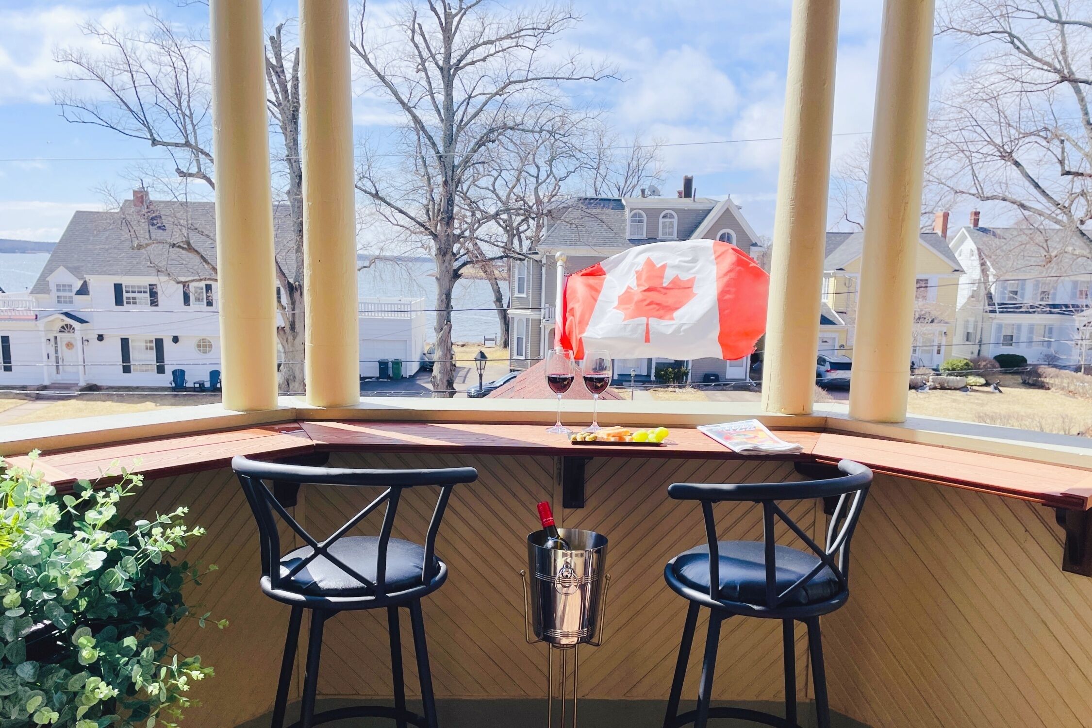 A covered outdoor seating area with two black chairs, a table with a bottle of wine, and a Canadian flag.