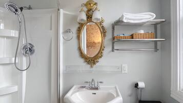 A bathroom with a shower, a sink, a mirror, and a towel rack.