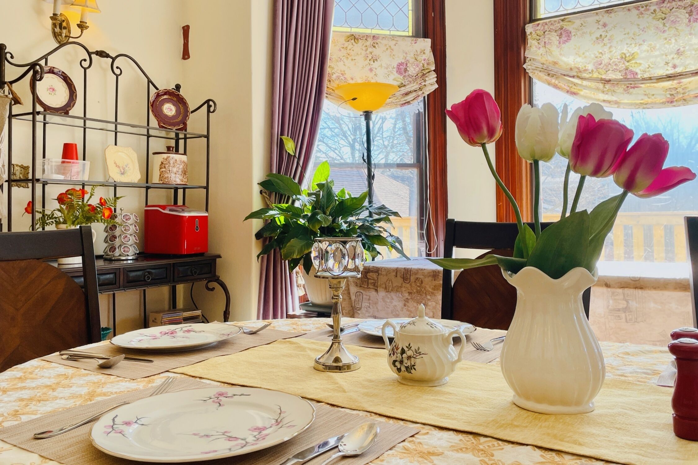 Een eettafel gedekt met borden, bestek, een vaas met bloemen en een lamp.