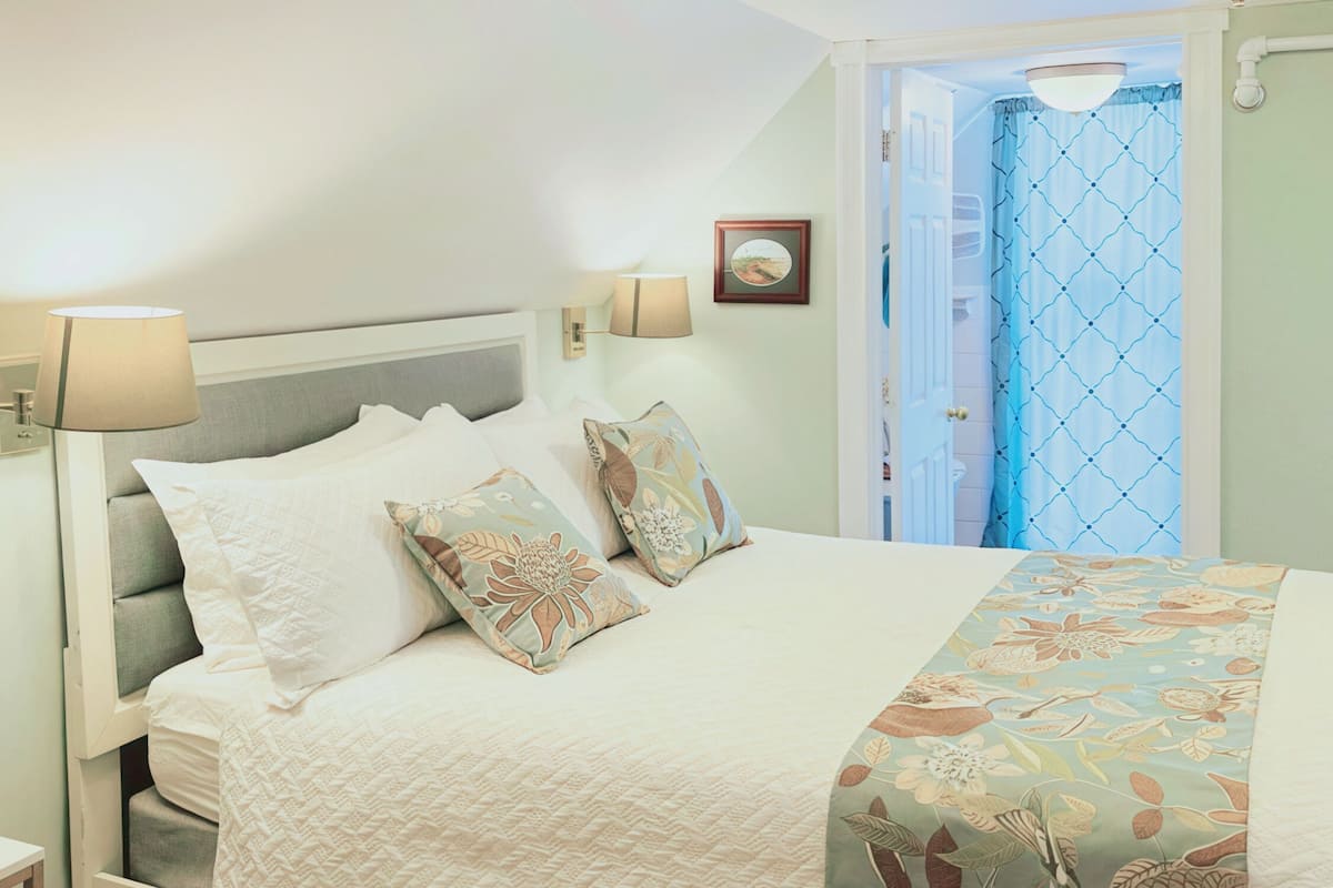 A neatly made bed with a floral-patterned bedspread and two decorative pillows. There are two wall-mounted lamps on either side of the bed.