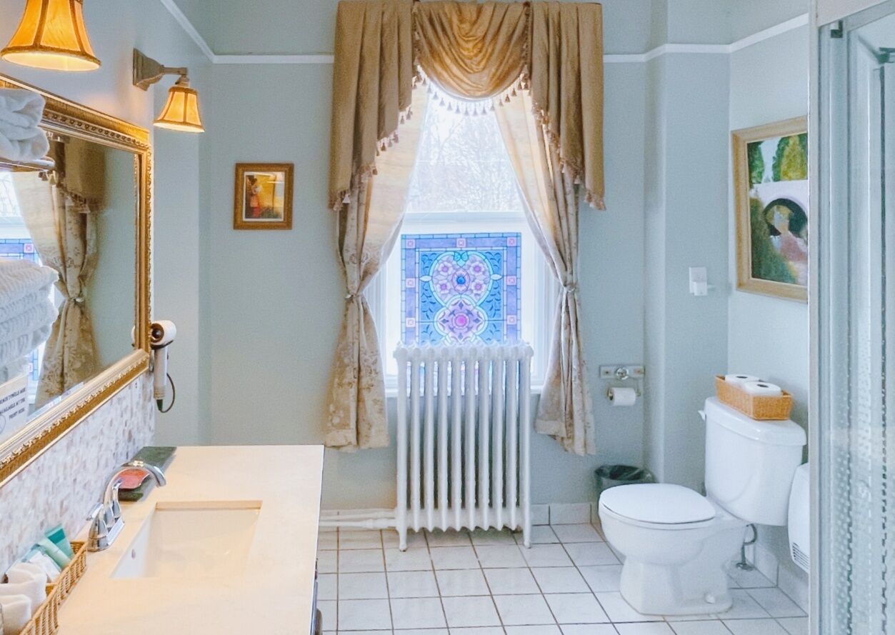 Un baño con un lavamanos blanco, un inodoro, un radiador y una ventana con vidrio decorativo.