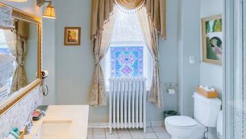 Un baño con un lavamanos blanco, un inodoro, un radiador y una ventana con vidrio decorativo.